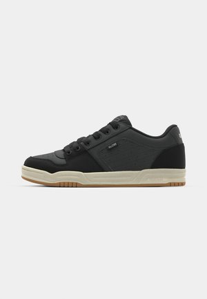 Black low-top sneaker with beige sole, lace-up front, perforated side panel, and "Globe" branding on side and heel.