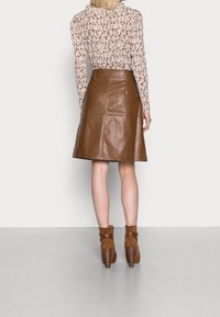 Bruine leren knie-lange rok met een gladde textuur, gecombineerd met een bloemige blouse met lange mouwen en bruine haklaarzen.