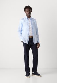 Lichtblauw, overhemd met lange mouwen en knoopsluiting, gedragen over een wit T-shirt. Gecombineerd met donkerblauwe broek en marineblauwe sneakers.