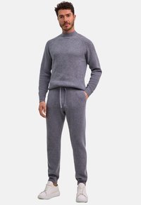 Szary, teksturowany sweter z wysokim kołnierzem, zestawiony z dopasowanymi spodniami dresowymi na sznurku. Noszony z białymi tenisówkami.