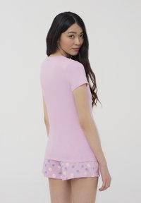 T-shirt rosa a maniche corte realizzata in tessuto morbido, abbinata a pantaloni corti rosa pastello con un motivo floreale in viola e bianco.