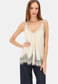 Kamisolka w kolorze kości słoniowej z koronkowym wykończeniem, głębokim dekoltem w kształcie litery V i falowanym dołem, zdobiona misternymi czarnymi koronkowymi akcentami oraz miękkim, lejącym się materiałem.