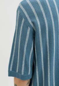 Pull en maille rayé bleu à manches courtes. Présente des rayures contrastantes gris clair et un tissu texturé, offrant une coupe décontractée.