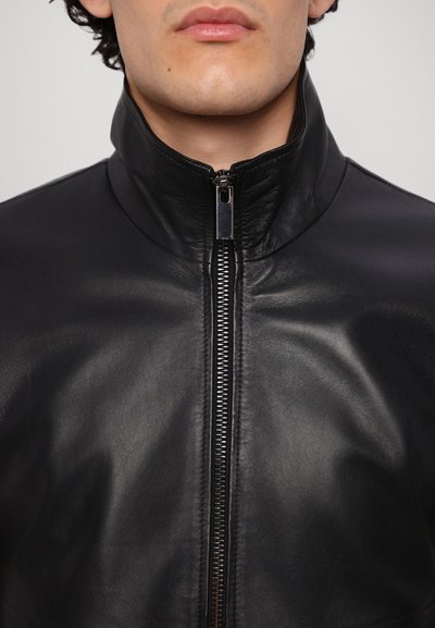 Black leather jacket with a high collar and front zipper. Smooth texture and fitted design, featuring a silver zipper and minimalistic style.