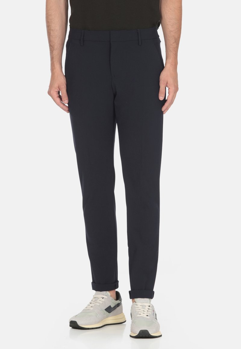 Pantaloni blu navy con vestibilità slim, realizzati in tessuto liscio, con vita piana e orli arrotolati, abbinati a sneaker sportive grigie chiare.