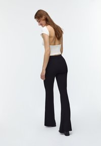 Bela skrajšana majica z odprtim hrbtom, v kombinaciji s črnimi širokimi hlačami. Gladek material, prilegajoč dizajn in diskretni šivi.