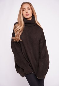 Übergroßer dunkelbrauner Strickpullover mit hohem Rollkragen und langen Ärmeln, der eine gerippte Textur und eine lockere Passform aufweist.