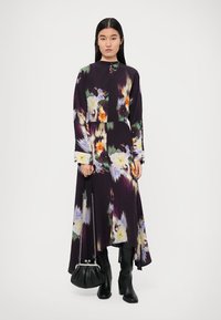 Long, dark purple dress with a floral pattern in various colors. Features long sleeves, a high neckline, and an asymmetrical hem.