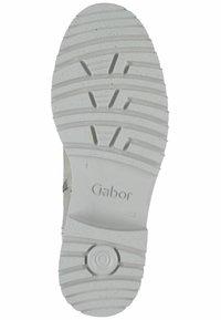 Semelle extérieure de chaussure en caoutchouc blanc avec des motifs de bande de roulement profonds et un accent circulaire. Marquée "Gabor", texturée pour une meilleure adhérence.