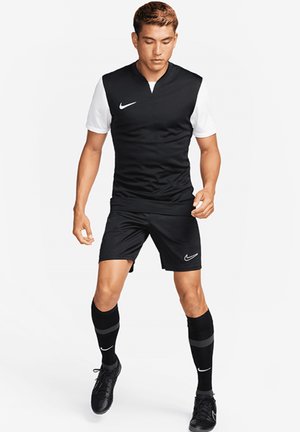 Zwarte Nike sportshirt met witte mouwen, zwarte shorts en zwarte sokken met grijze accenten; bevat een Nike-logo op de borst en op de sokken.
