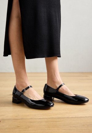 Zapatos Mary Jane de charol negro con un tacón bajo y correa en el tobillo, con una punta redondeada y un acabado suave y brillante.