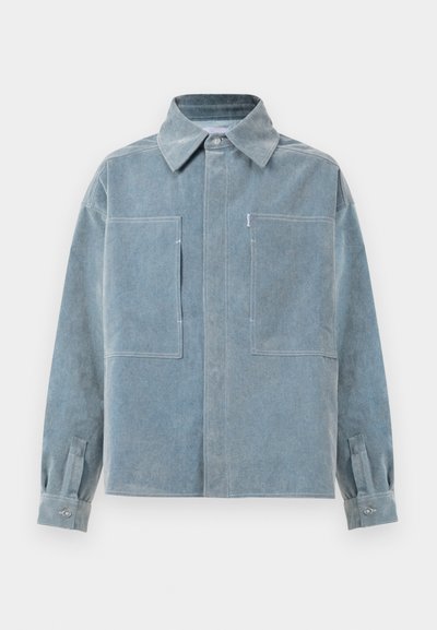 Heled sinine teksajakk kraega, kahe rinnaehtsusega taskuga, pikkade varrukatega ja nööpidega mansettidega. Kätkub peeneid õmblusdetailide.