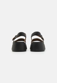 Sorte plattform sandaler i svart med to justerbare stropper, glatt lærtekstur og en bred, chunky hæl. Sålen har en teksturert overflate.