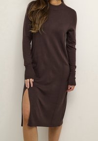 Robe marron à manches longues avec un col rond, des poignets côtelés et une fente sur le côté jusqu'à la cuisse. Fabriquée en matériau lisse et extensible.
