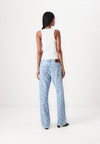Lichtblauwe jeans met een all-over patroon, losse pasvorm en een leren label op de tailleband. Gecombineerd met een aangesloten witte tanktop.