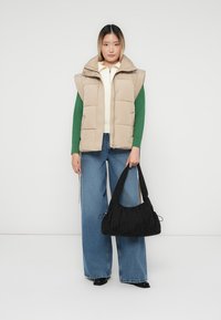 Bežna podložena jakna preko zelene svetre, v kombinaciji s svetlo modrimi širokimi hlačami in črno teksturirano torbico z vrvico.