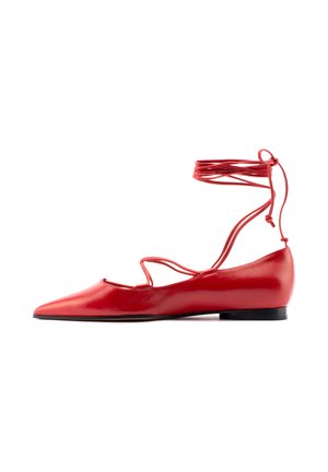 Scarpa piatta rossa con punta a punta appuntita e sottili cinturini incrociati alla caviglia che si avvolgono e si legano sopra la caviglia.