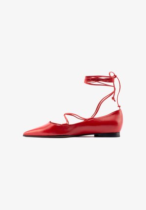Scarpa piatta rossa con punta a punta appuntita e sottili cinturini incrociati alla caviglia che si avvolgono e si legano sopra la caviglia.