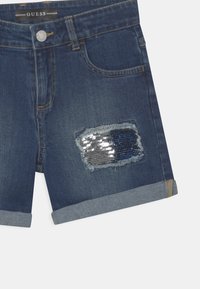 Shorts de mezclilla en azul oscuro con un dobladillo deshilachado, que cuentan con un parche de lentejuelas azules en una pierna y un diseño clásico de cinco bolsillos.