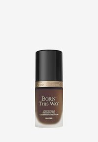 Bruine glazen foundationfles met een zwarte dop en gouden accenten. Etiket luidt "Born This Way, Undetectable Medium-to-Full Coverage Foundation."