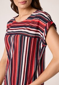 Pasiasty t-shirt z krótkim rękawem w kolorach czerwonym, białym i granatowym, z okrągłym dekoltem i luźnym krojem. Miękka tkanina z pionowymi paskami.