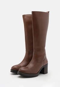 Bottes en cuir marron montantes jusqu'au genou avec un bout arrondi et un talon carré. Présentent une texture lisse et une couture contrastante le long des coutures.