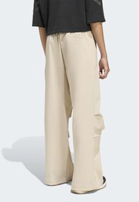 Béžové široké kalhoty s hladkou texturou, elastickým pasem a bočními kapsami, spárované s černým krátkým topem.