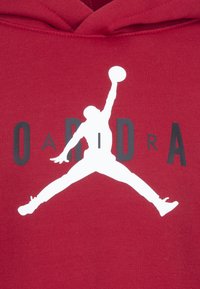 Sudadera roja con capucha que presenta una gran silueta blanca de una figura saltando, una pelota de baloncesto y el texto "AIR" en letras grises. Material de algodón con un acabado texturizado.
