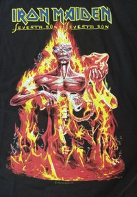 Černé bavlněné tričko s grafikou svalnaté červené postavy uprostřed plamenů, která drží lebku a meč. Text zní "Iron Maiden Seventh Son."