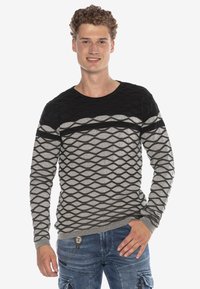 Schwarzer und grauer, gemusterter Pullover mit einem strukturierten Rautendesign, Rundhalsausschnitt und gerippten Bündchen, kombiniert mit blauen Cargo-Hosen.