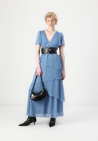Rochie maxi cu buline albastre, cu volane stratificate, baretă lată neagră și o geantă mică neagră. Modelul poartă booties negre cu toc ascuțit.
