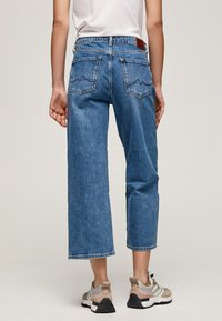 Ljusblå denim culotte-jeans med hög midja, fem fickor och ett distinkt vågmönster på bakfickorna.