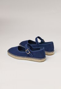 Navy blue suede shoes with a round toe and ankle strap, featuring a jute sole with braided detailing along the edge.