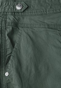 Dark green fabric featuring a textured surface, with a metal snap button and detailed stitching along the edges and pockets.