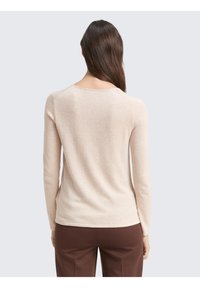 Pull beige à manches longues avec un col rond, une texture côtelée et une coupe ajustée, porté avec un pantalon marron.