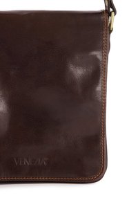Brązowa skórzana torba na ramię o gładkiej fakturze, zaokrąglonym kształcie i kontrastowym przeszyciu; posiada wytłoczone logo marki "VENEZIA."