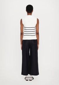 Top en tricot blanc léger sans manches avec des rayures horizontales bleu marine, associé à un pantalon large noir. Matériau texturé avec des accents côtelés.