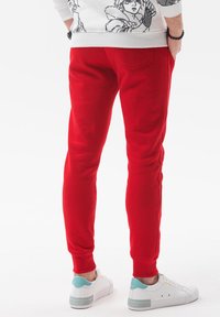 Røde sweatpants med en slim fit, ribbede manchetter og en baglomme. Parret med hvide sneakers med et lyseblåt accent.