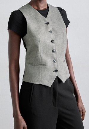 Slim fit grijze knoopjesvest gedragen over een zwarte top met korte mouwen en gecombineerd met zwarte hoge taille broek.