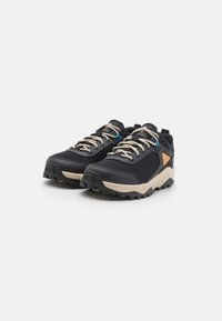 Chaussures de randonnée en mesh noir avec des accents beiges, semelles texturées et lacets ronds. Caractéristiques incluant un œillet bleu et un design de soutien.