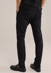 Fekete, slim fit nadrág, elülső zsebekkel és sima textúrával, fekete lakkcipőkkel párosítva. Egyszerű dizájn, nincs látható minta.