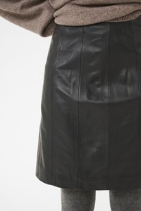 Falda de cuero negro con una textura suave y costuras verticales. Combinada con medias grises texturizadas, el diseño es simple y elegante.
