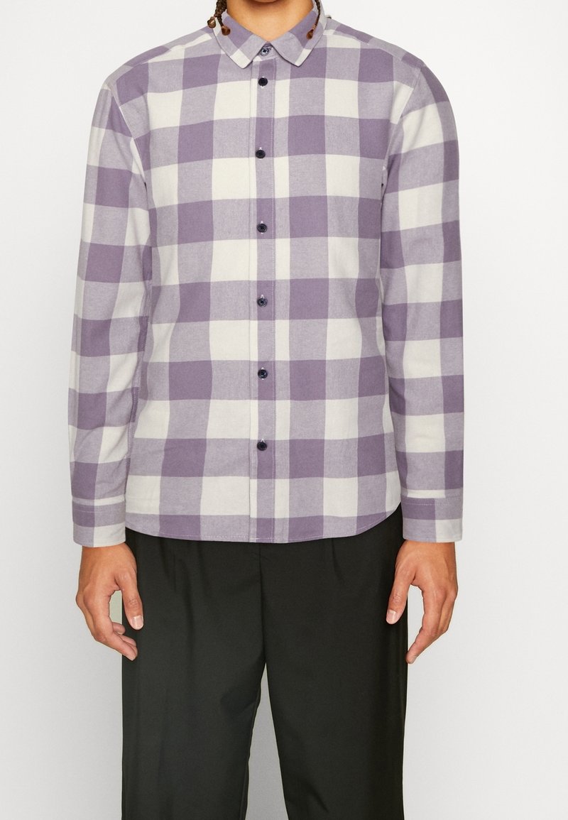 Lila en witte geruite blouse met lange mouwen en een kraag, knoopsluiting aan de voorkant en zwarte knopen. De stof heeft een zachte textuur en een ontspannen pasvorm.