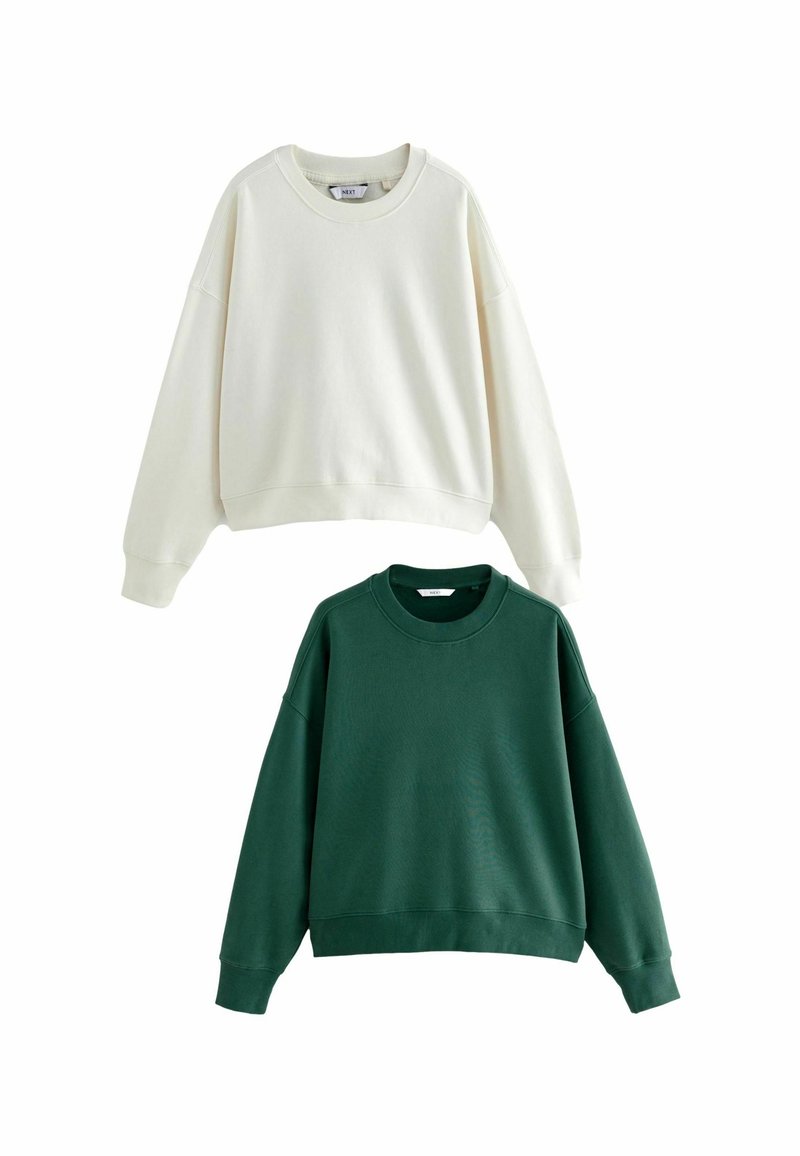 Twee sweaters: de ene crème, de andere donkergroen. Beide hebben een ronde hals, verlaagde schouders en ribgebreide boorden. Zachte katoenmix.
