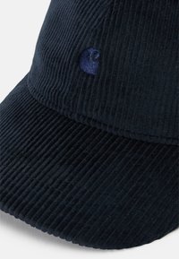 Gorra de pana en color azul marino con una superficie texturizada, presenta un logotipo azul elevado en la parte frontal y una visera estructurada.