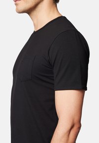 Czarna bawełniana koszulka z okrągłym dekoltem, krótkimi rękawami i kieszenią na piersi. Charakteryzuje się gładką fakturą i dopasowanym krojem.