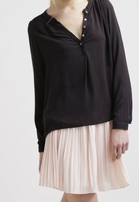 Top nero a maniche lunghe con scollo a V e bottoni, abbinato a una gonna plissettata rosa chiaro. Tessuto morbido con una vestibilità comoda.