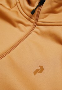 Orange zip-hoodie med glat, mat stof. Har et diagonalt logo i en mørkere nuance og kontrasterende lynlåsdetaljer.