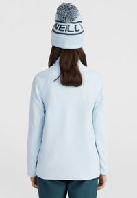 Veste en polaire bleu clair avec un col montant et des manches longues ; accompagnée d'un bonnet en tricot avec un pompon et un design textuel contrasté.
