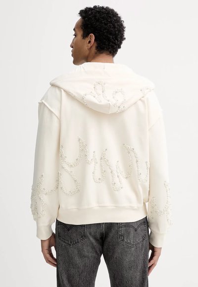 Felpa bianca con cappuccio caratterizzata da decorazioni testurizzate a motivi ondulati sul retro, dotata di cappuccio regolabile e vestibilità rilassata.